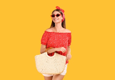 Photo of Beautiful young woman with stylish straw bag on yellow background