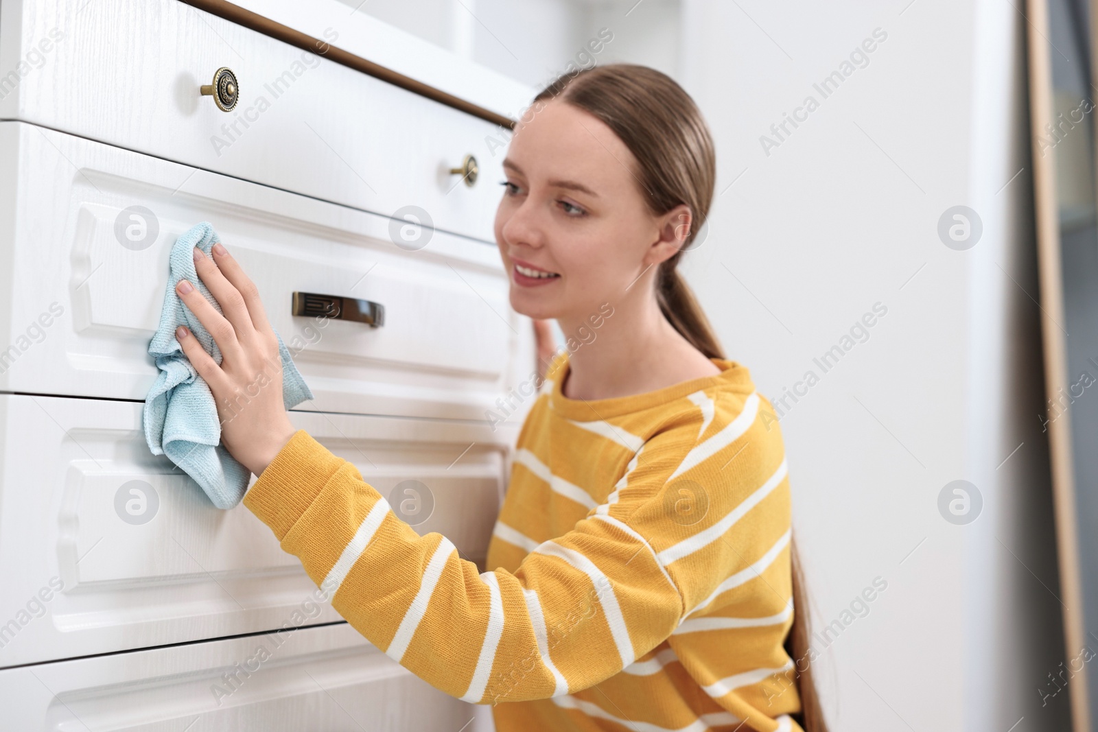 Photo of Woman cleaning chest of drawers with rag at home