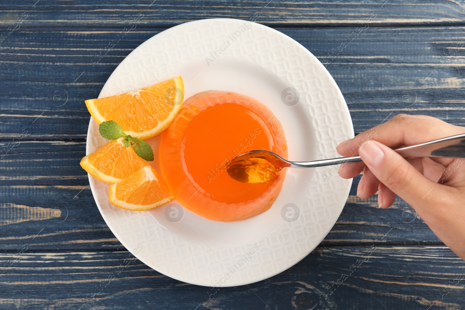 Photo of Young woman eating tasty orange jelly at blue wooden table, top view