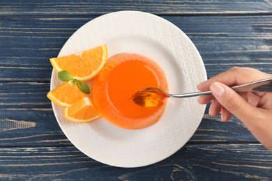 Young woman eating tasty orange jelly at blue wooden table, top view