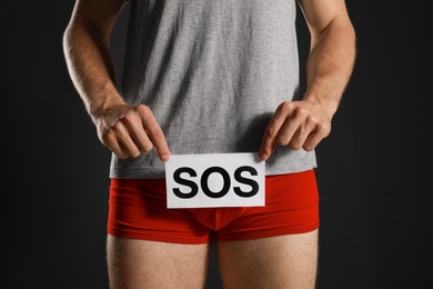 Photo of Man holding SOS sign on black background, closeup. Urology problems