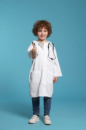 Little boy in medical uniform showing thumbs up on light blue background