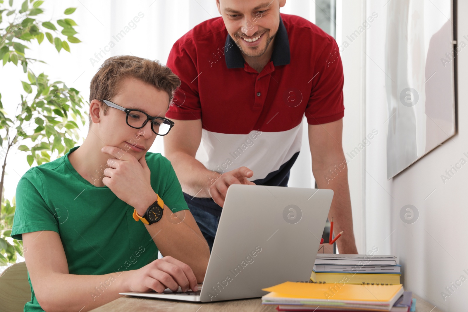 Photo of Father helping his teenager son with homework indoors