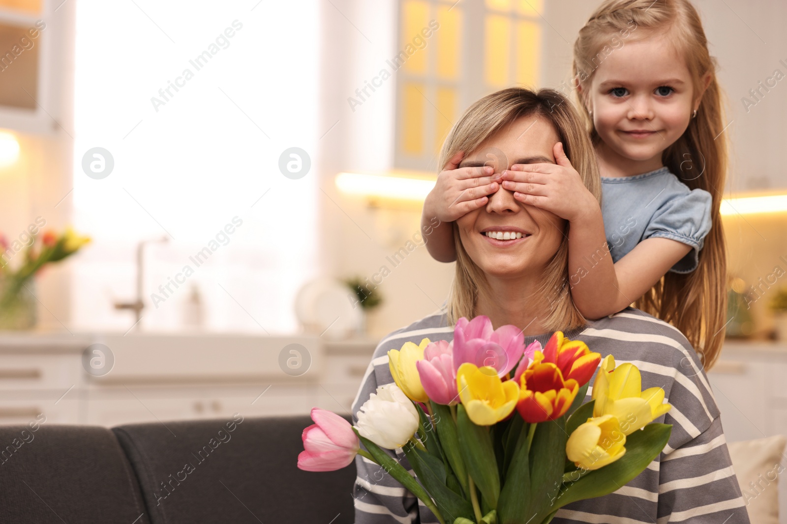 Photo of Little girl surprising her mom with bouquet of tulips at home, space for text. Happy Mother`s Day