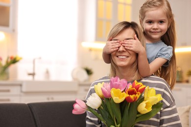 Little girl surprising her mom with bouquet of tulips at home, space for text. Happy Mother`s Day