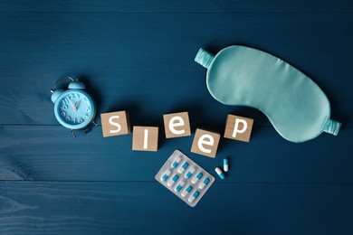 Photo of Word Sleep, alarm clock, pills and mask on blue wooden table, flat lay. Insomnia treatment
