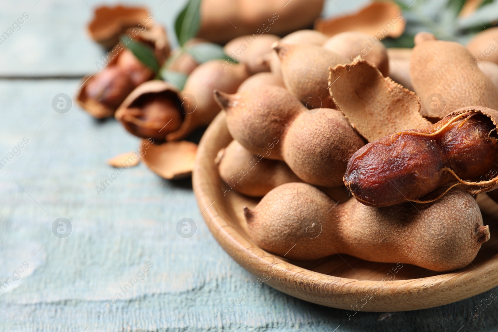 Photo of Plate with delicious ripe tamarinds on blue wooden table, closeup. Space for text