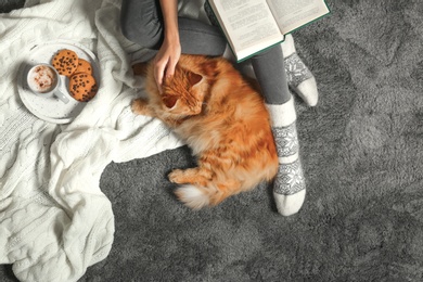 Woman with cute red cat and book on grey carpet, top view