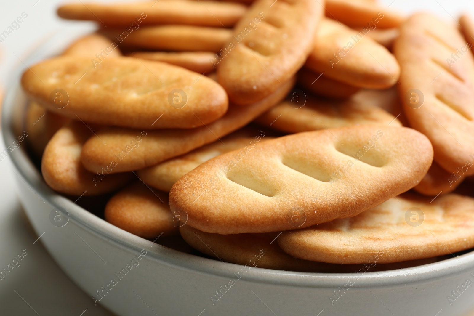 Photo of Delicious crispy crackers in bowl, closeup view