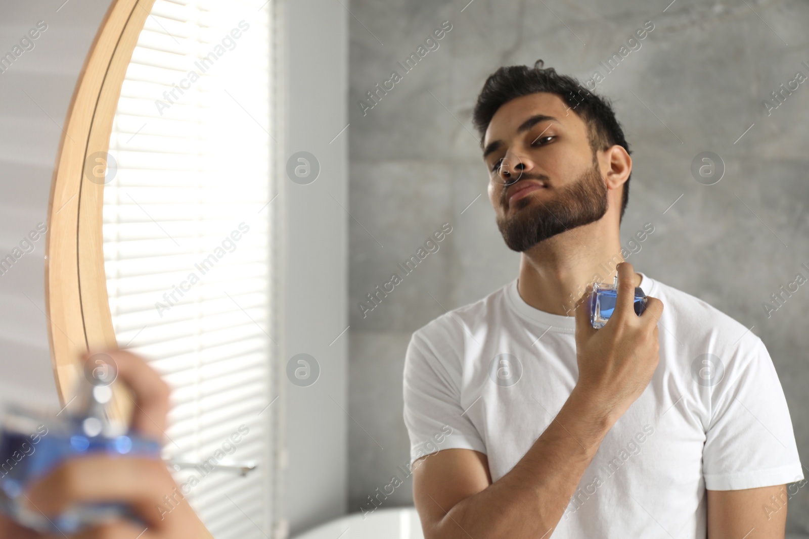 Photo of Man spraying luxury perfume near mirror indoors