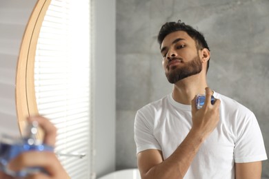 Man spraying luxury perfume near mirror indoors