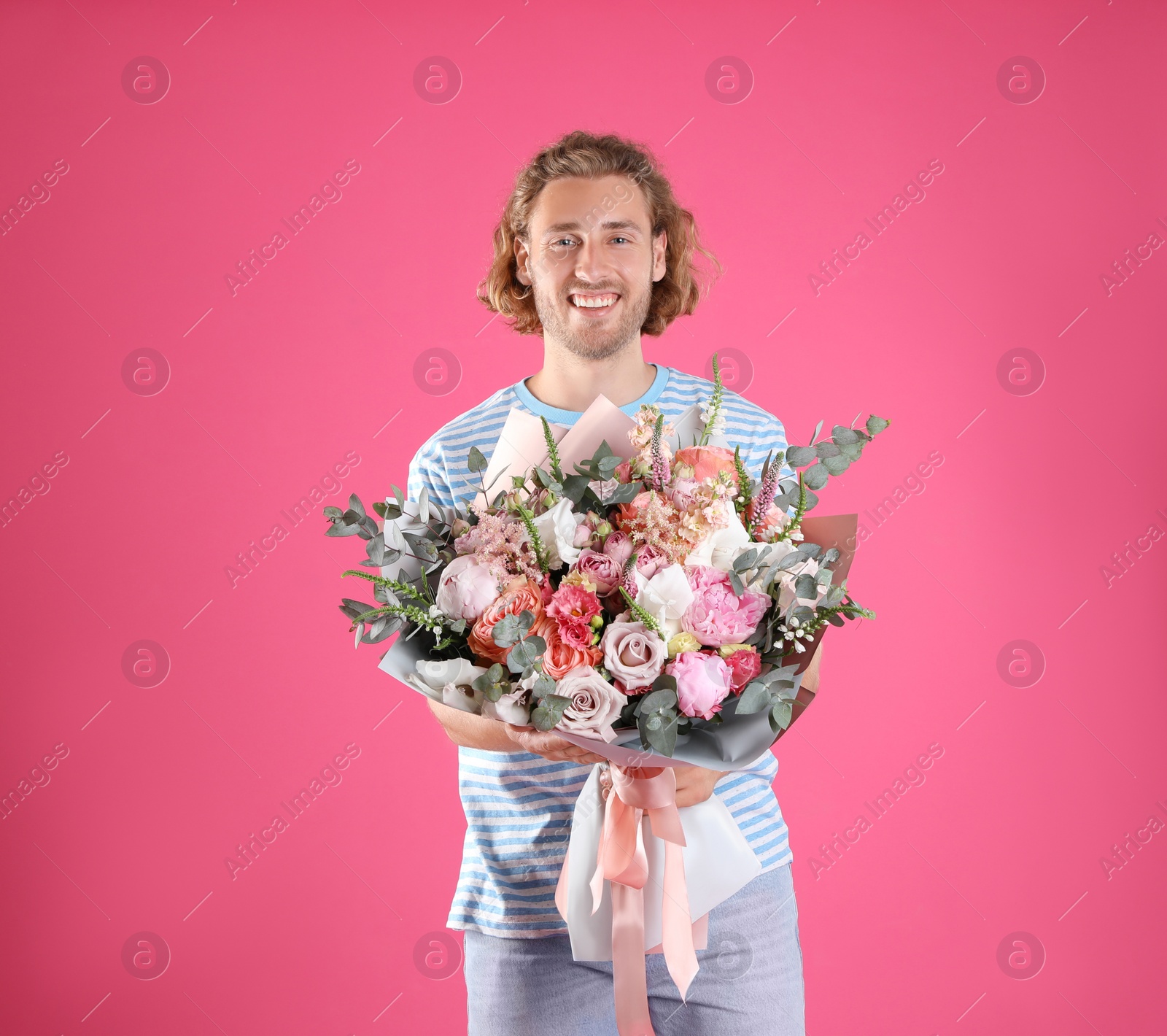 Photo of Young handsome man with beautiful flower bouquet on pink background