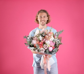 Young handsome man with beautiful flower bouquet on pink background
