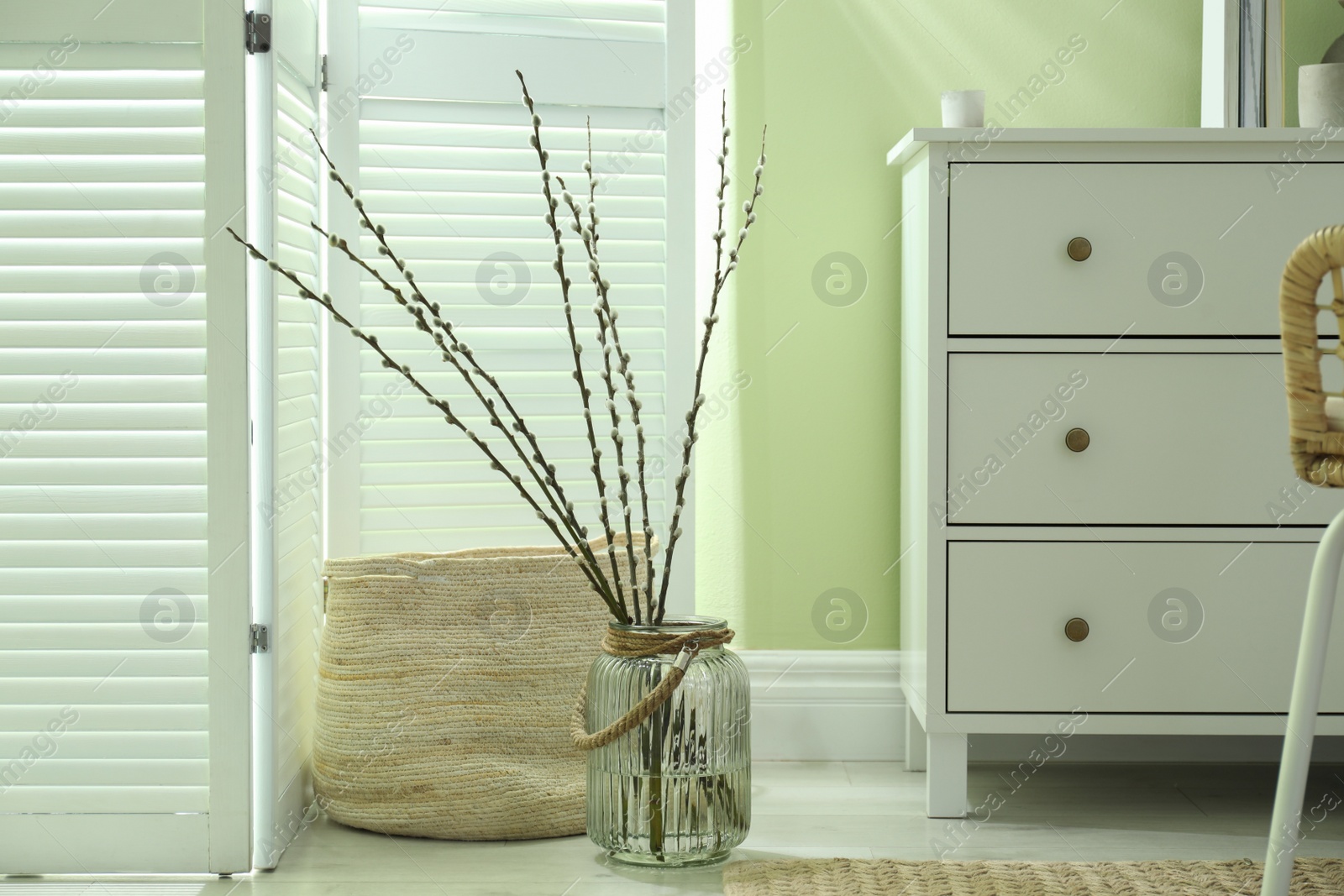 Photo of Glass vase with pussy willow tree branches on floor in room