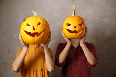 Photo of Women with pumpkin heads against beige background. Jack lantern - traditional Halloween decor