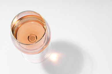 Rose wine in glass and shadow on white background, top view. Space for text