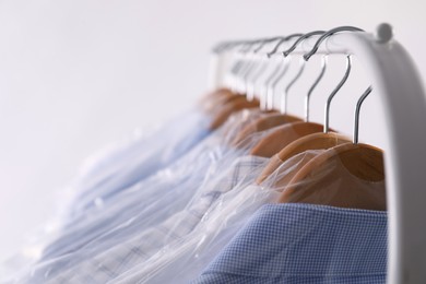 Photo of Hangers with shirts in dry cleaning plastic bags on rack against light background, closeup. Space for text
