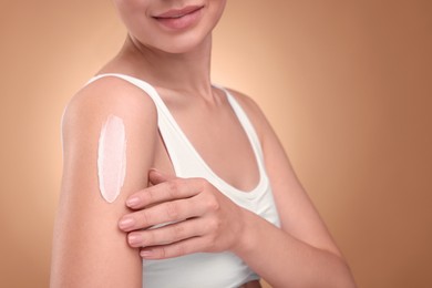 Woman with smear of body cream on her shoulder against light brown background, closeup. Space for text