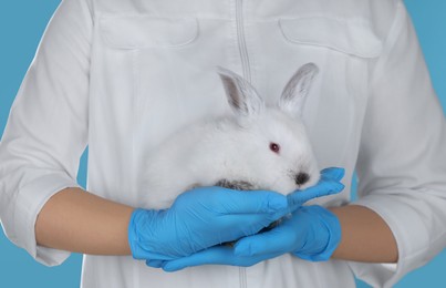 Scientist holding rabbit on light blue background, closeup. Animal testing concept
