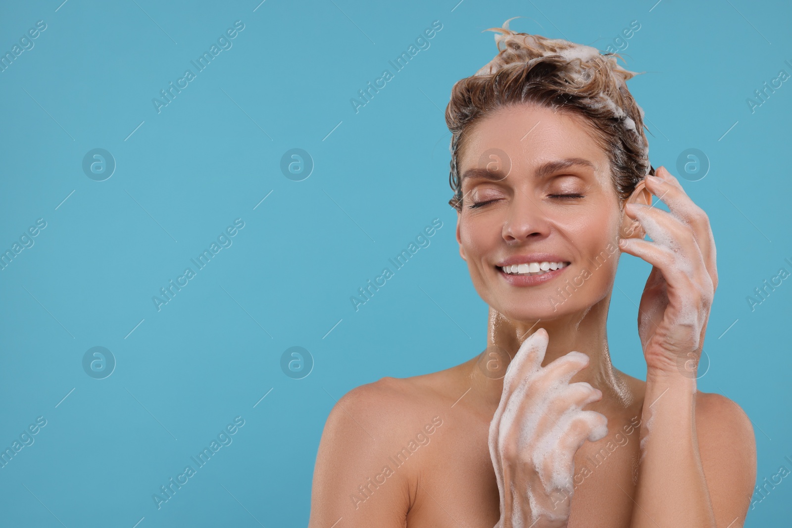 Photo of Beautiful happy woman washing hair on light blue background. Space for text