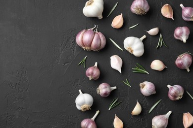 Photo of Fresh garlic and rosemary on dark textured table, flat lay. Space for text