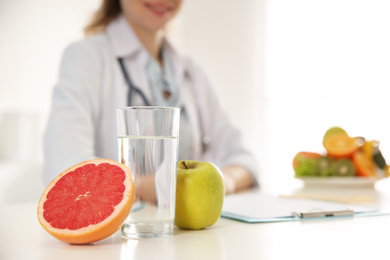 Photo of Glass of water, fresh fruits and blurred nutritionist on background