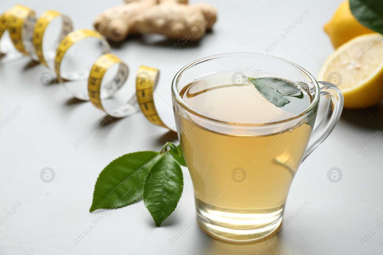 Photo of Herbal diet tea, lemon, ginger and measuring tape on light table