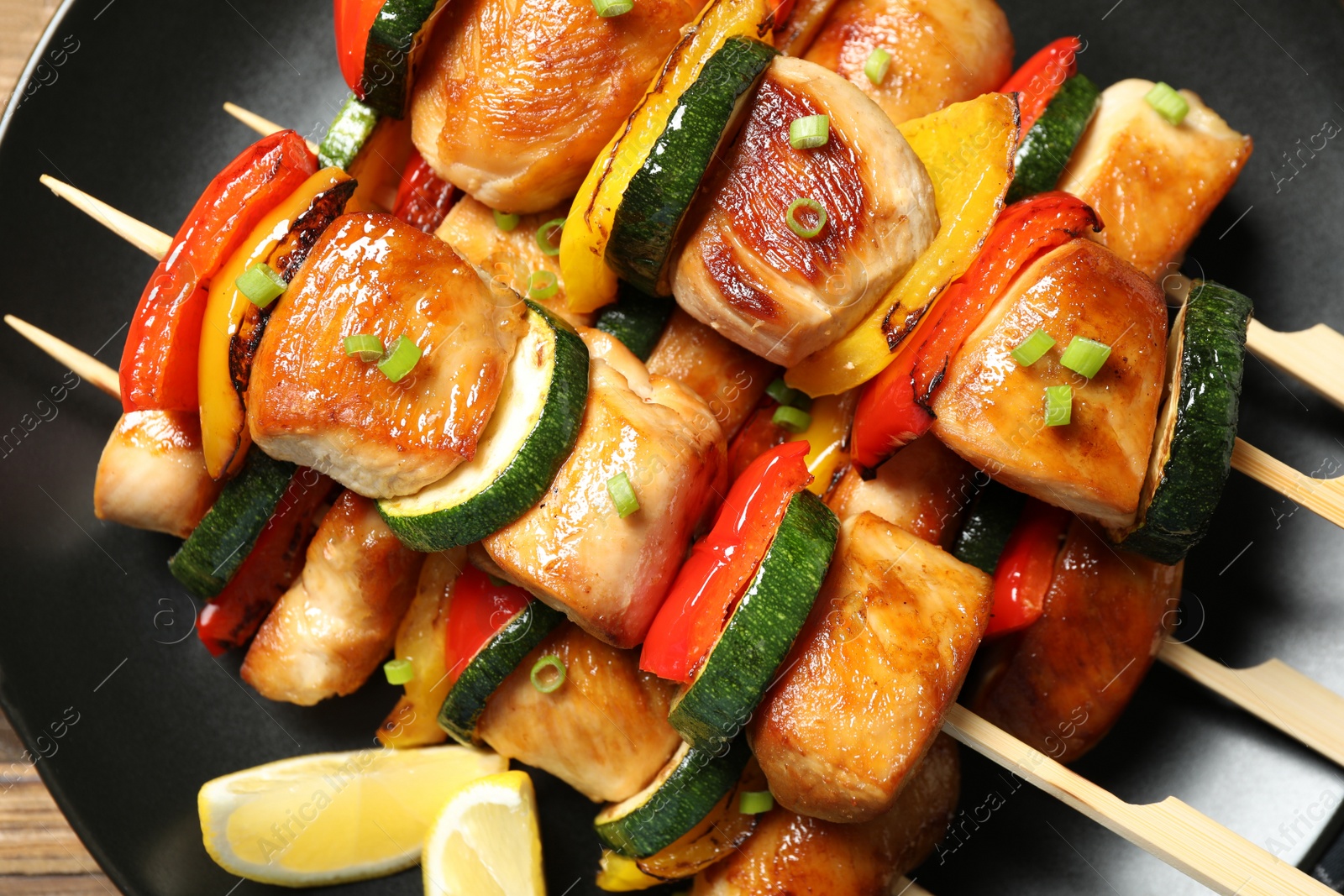 Photo of Delicious chicken shish kebabs with vegetables and lemon on plate, top view