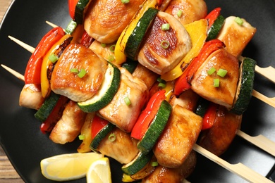 Delicious chicken shish kebabs with vegetables and lemon on plate, top view