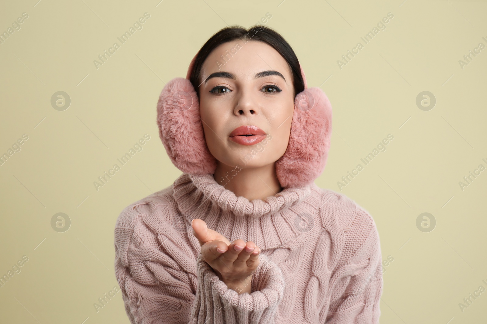 Photo of Beautiful young woman wearing earmuffs on beige background