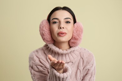 Beautiful young woman wearing earmuffs on beige background