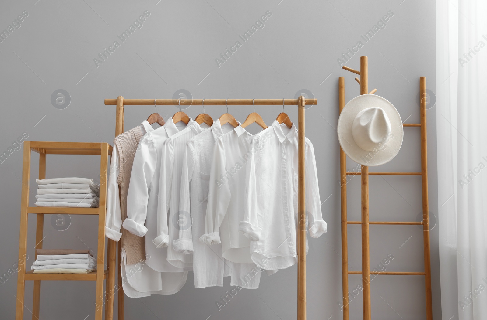 Photo of Wardrobe organization. Rack with different stylish clothes, hat, ladder and shelving unit near grey wall