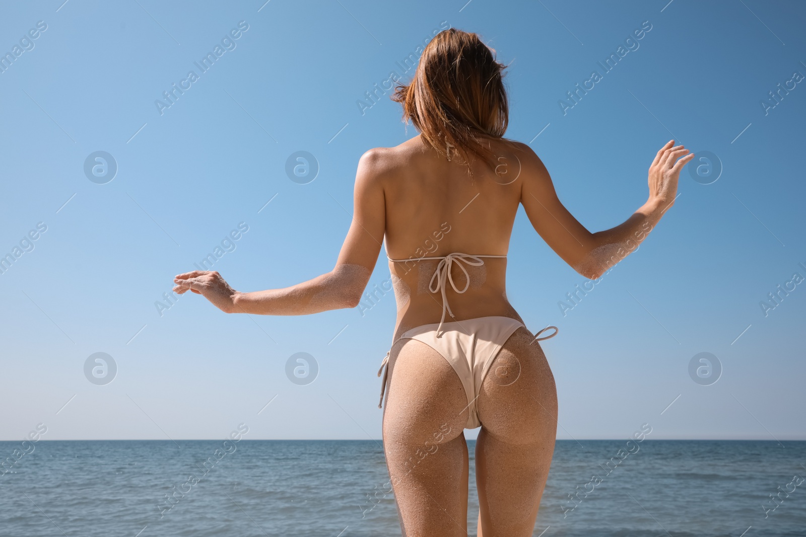 Photo of Woman with sand on perfect body in bikini near sea, back view