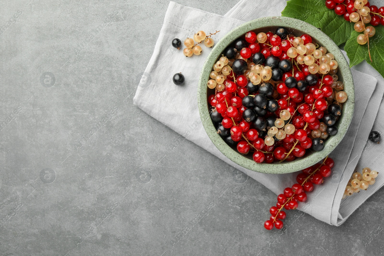 Photo of Different fresh ripe currants and green leaves on light grey table, flat lay. Space for text