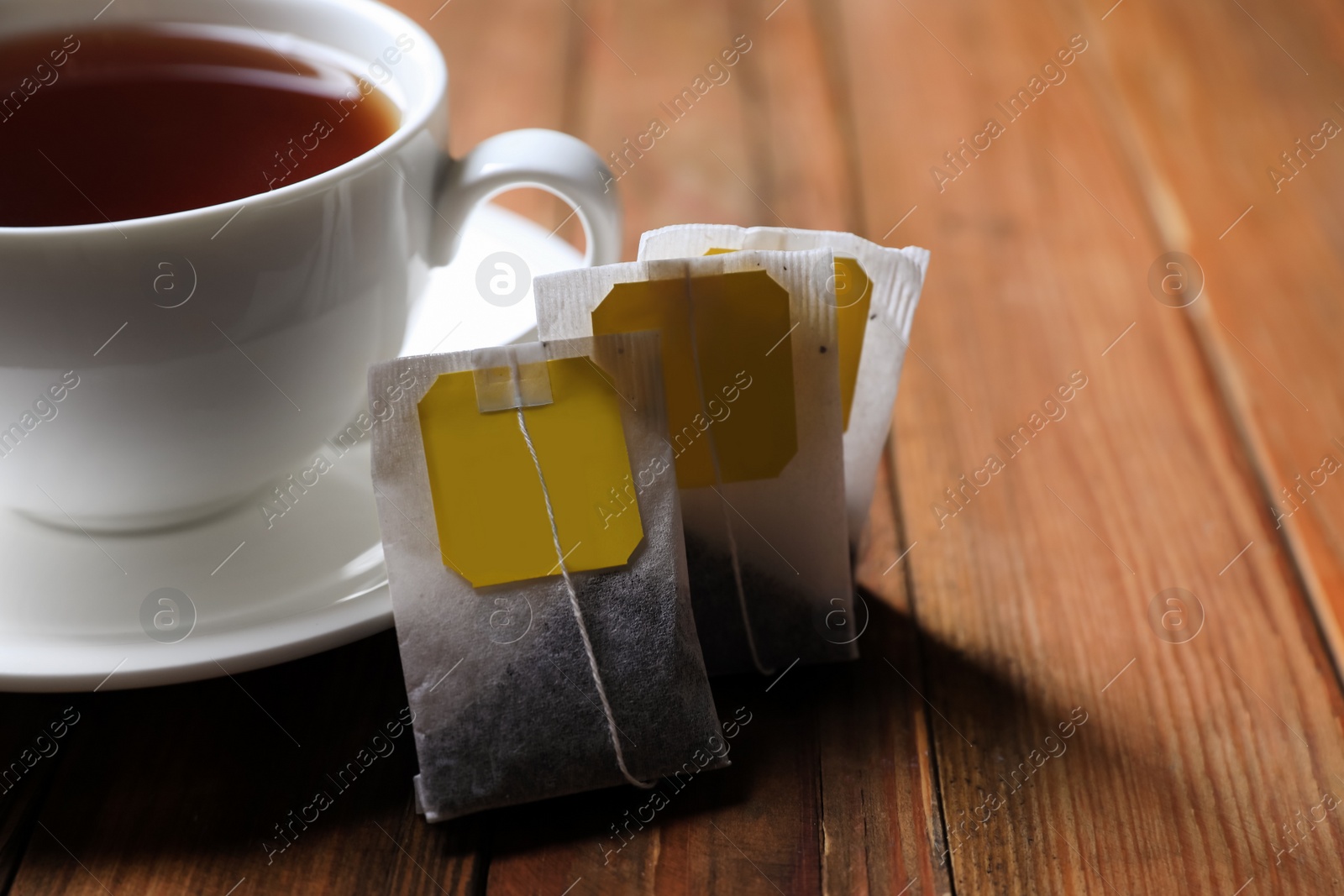 Photo of Tea bags near cup of hot drink on wooden table, closeup