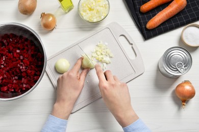 Photo of Woman cutting onion at white wooden table, top view. Cooking vinaigrette salad
