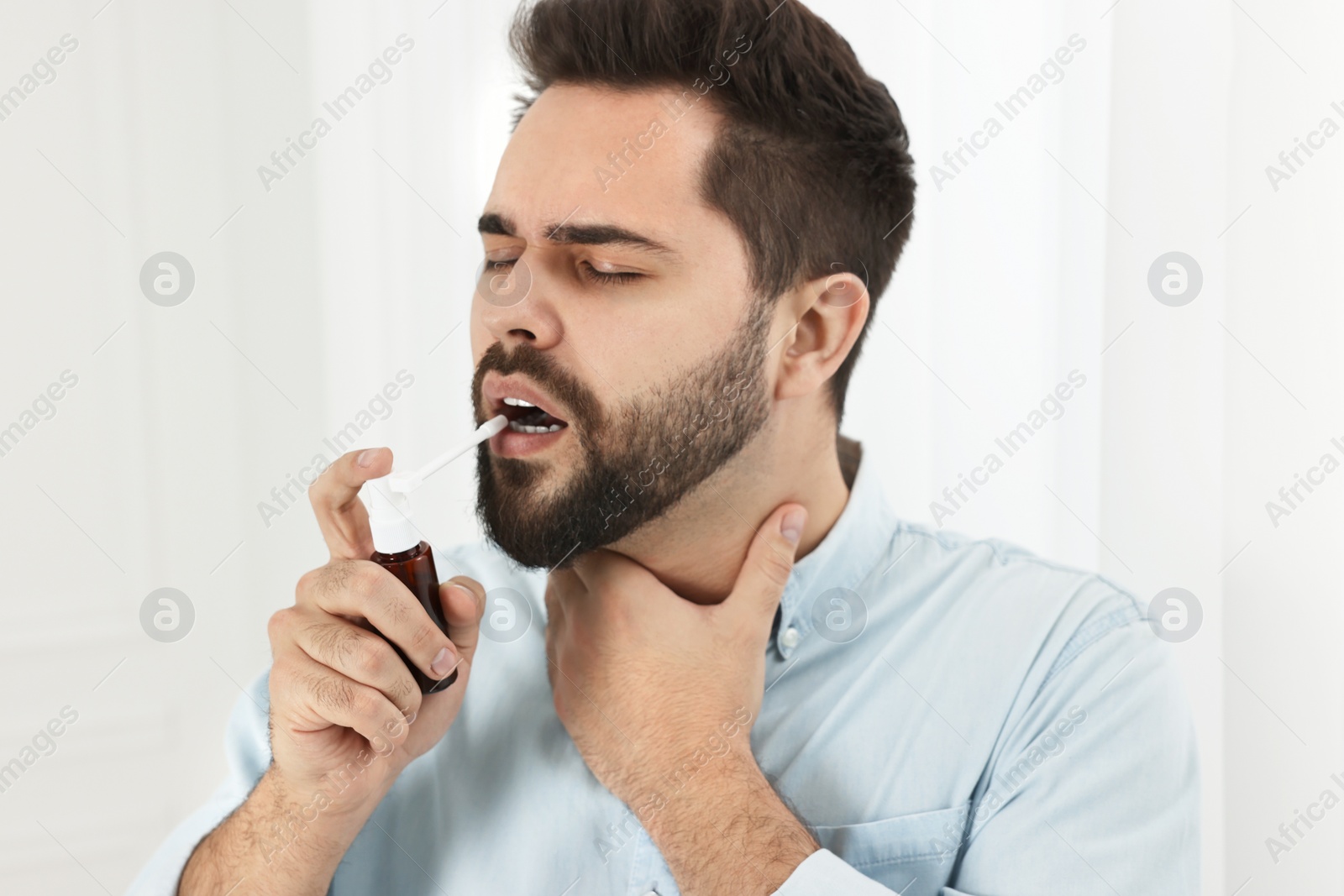 Photo of Young man using throat spray at home