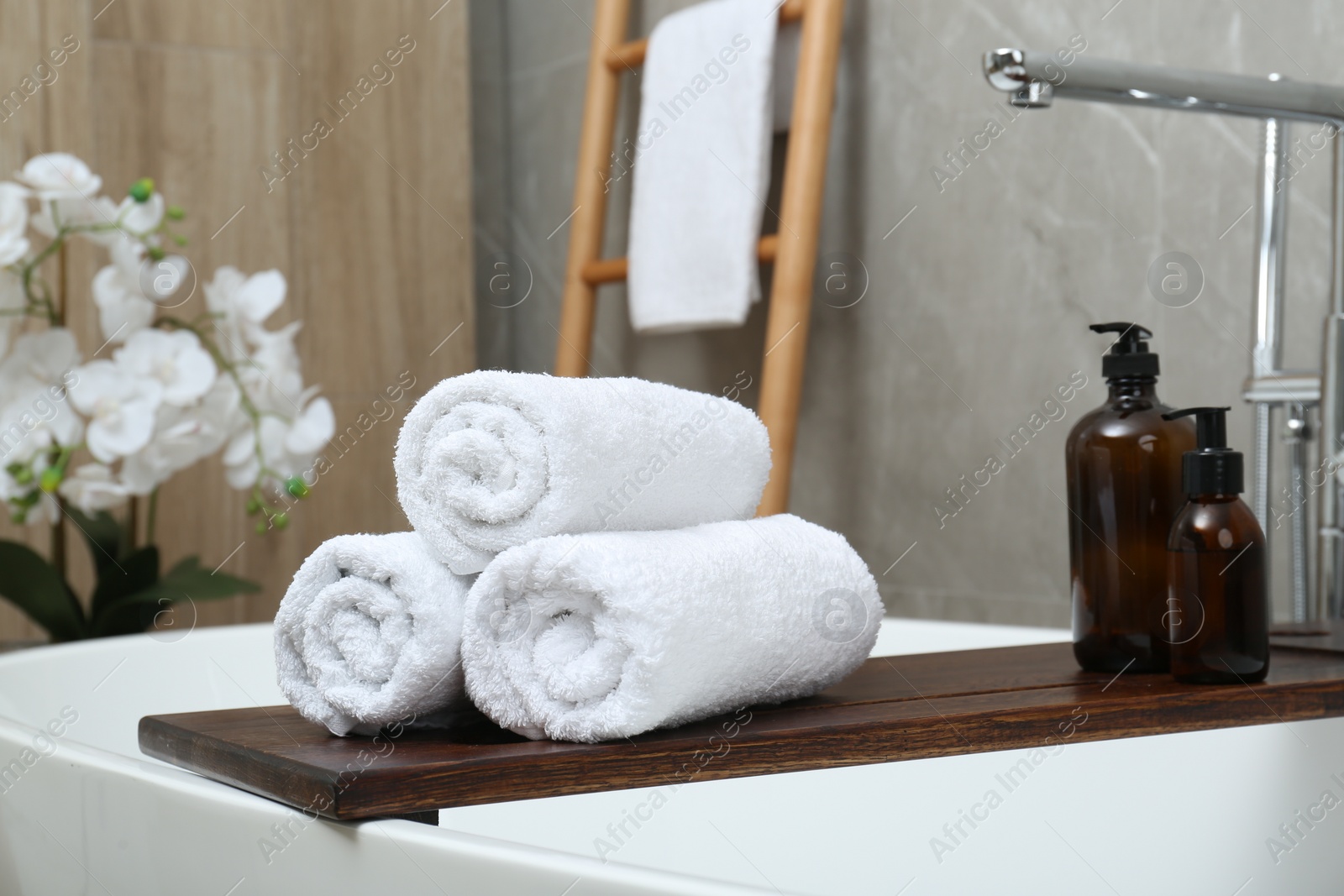 Photo of Rolled towels and personal care products on tub tray in bathroom