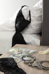 Photo of Prostitution concept. Handcuffs, black panties, dollar banknotes and condom on wooden table indoors, closeup
