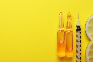 Photo of Pharmaceutical ampoules with medication, syringe and citrus slices on yellow background, flat lay. Space for text