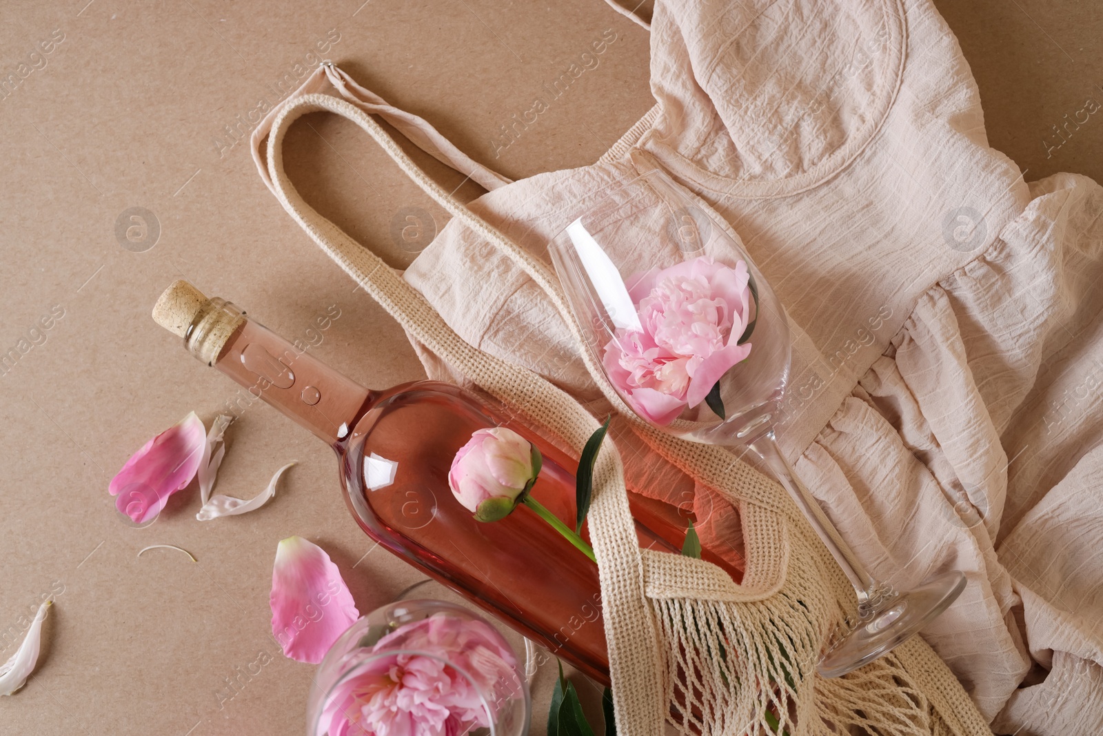 Photo of Flat lay composition with rose wine, mesh bag, dress and beautiful pink peonies on brown background