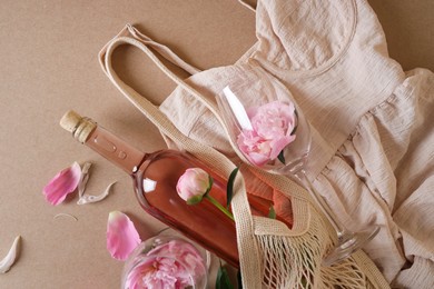 Photo of Flat lay composition with rose wine, mesh bag, dress and beautiful pink peonies on brown background