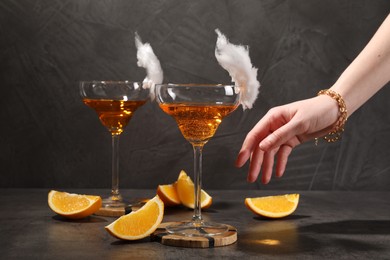 Photo of Woman taking tasty cocktail in glass decorated with cotton candy at gray table, closeup