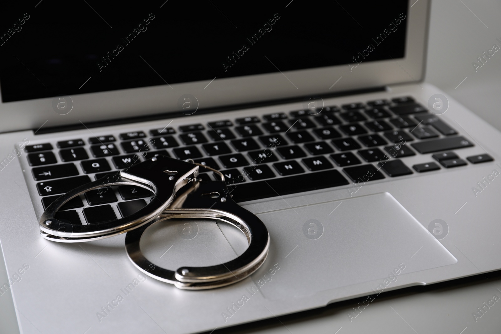 Photo of Laptop and handcuffs on table, closeup. Cyber crime