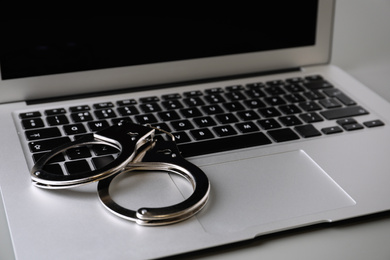 Photo of Laptop and handcuffs on table, closeup. Cyber crime