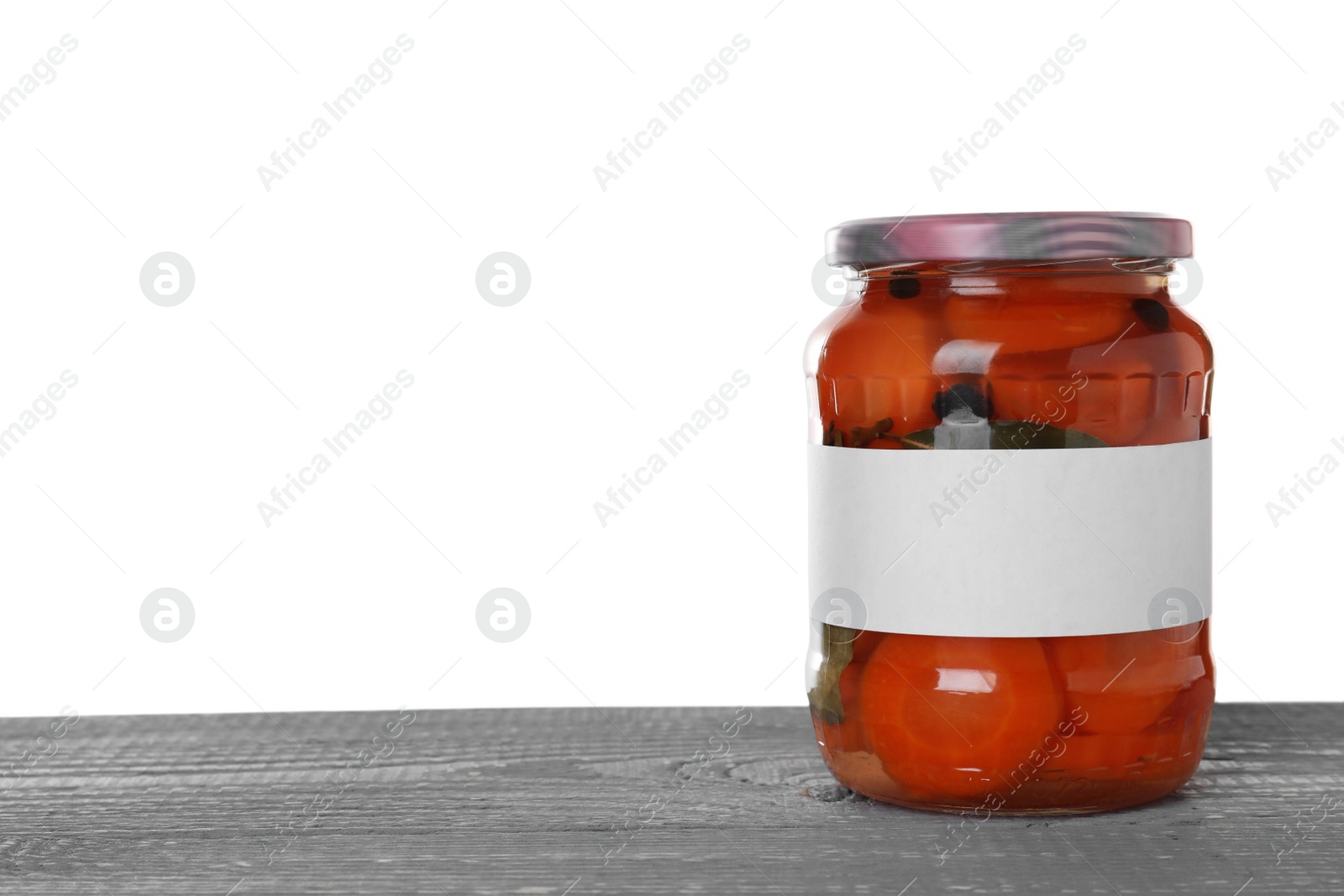 Photo of Jar of pickled sliced carrots with blank label on blue wooden table against white background. Space for text