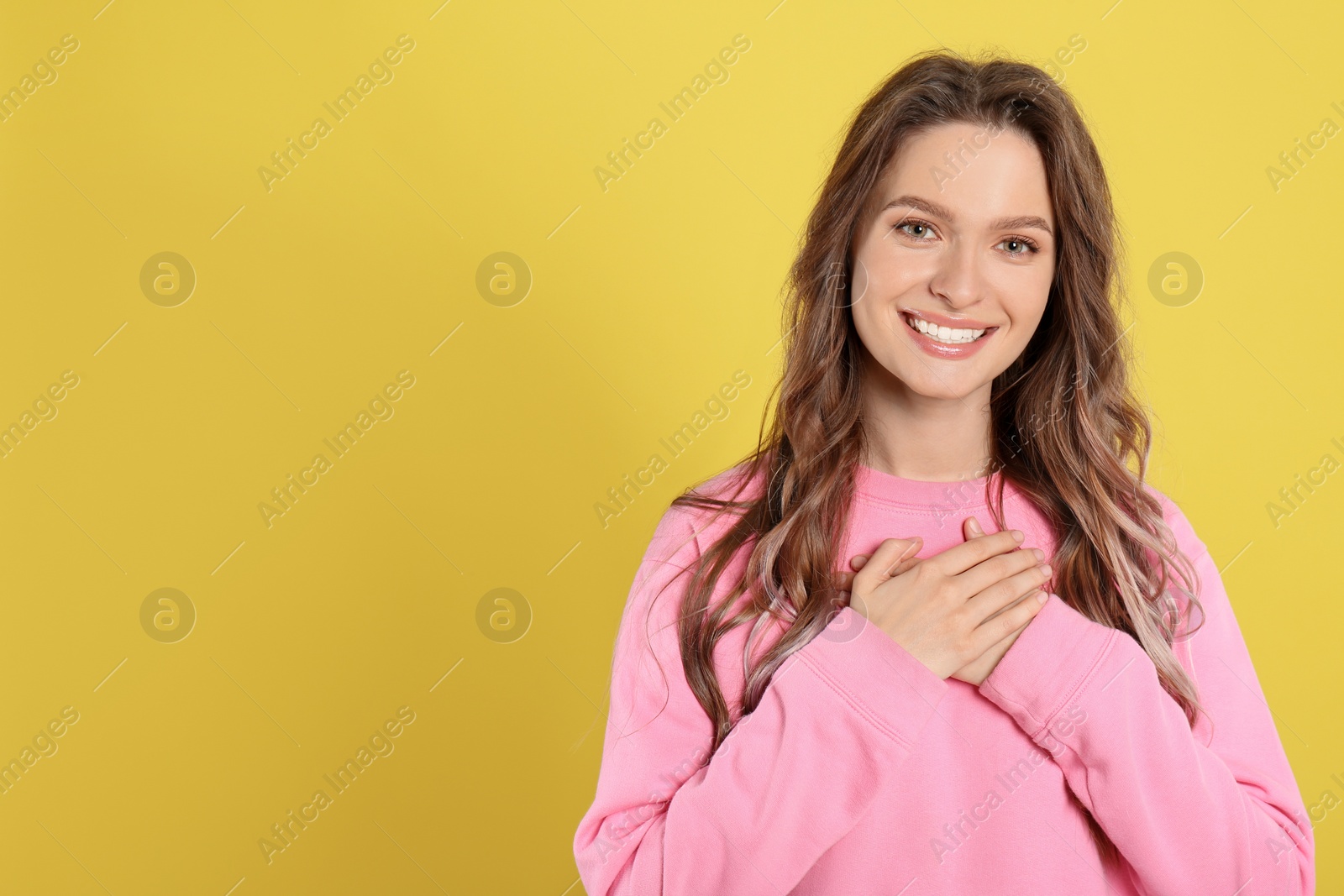 Photo of Beautiful grateful woman with hands on chest against yellow background. Space for text