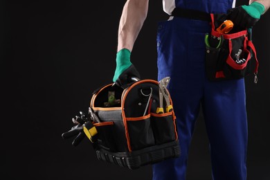 Professional repairman with tool box on black background