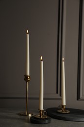Photo of Elegant candlesticks with burning candles on grey table