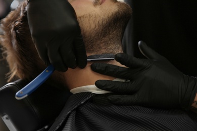 Photo of Professional hairdresser shaving client with straight razor in barbershop